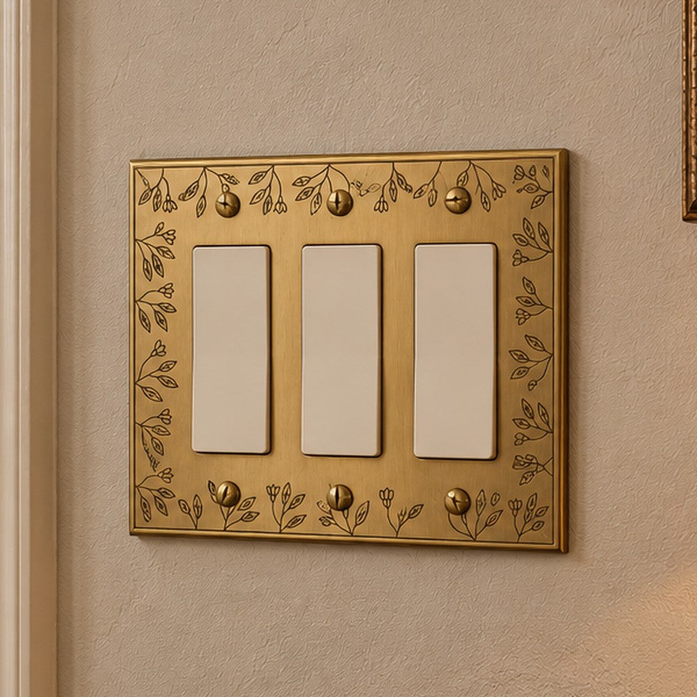Floral Brushed Gold 3-gang rocker switch plate on a wall beside a wood staircase railing.
