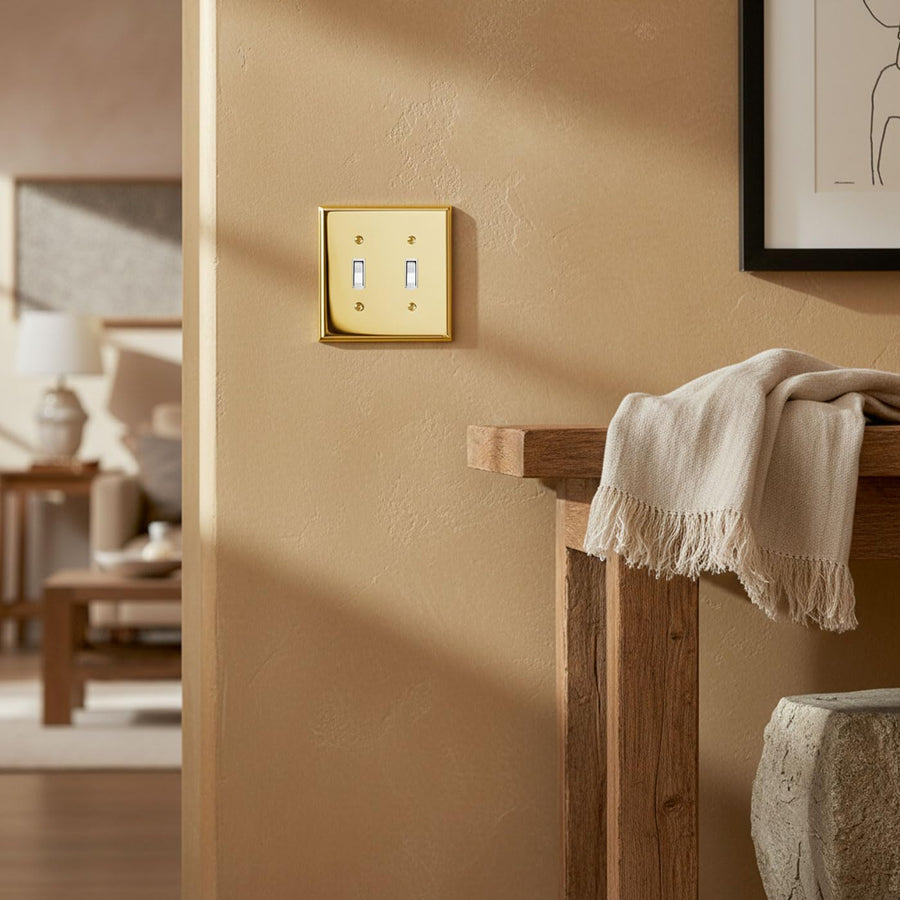Signature 2-gang toggle switch plate in Polished Gold on a warm wall above a towel on a wood stand