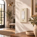 A Forge 1G Rocker switch plate in Warm Ivory with Gold screws on a creamy wall in morning light