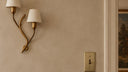 Brass-toned toggle switch plate on a warm plaster hallway wall beside a brass sconce and wooden console with flowers.