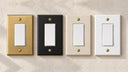 Forge rocker switch plates in Brushed Gold, Black, Warm Ivory, and White with gold screws on a textured white wall.
