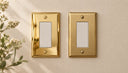 Polished Gold and Brushed Brass Signature rocker plates side by side on a warm plaster wall.