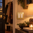 Signature Polished Gold 2-gang rocker switch plate by an entry with coats, a glowing lamp, and greenery