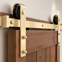 Close-up of a Light Gold barn door hanger and black roller on the rail, mounted on a dark wood door