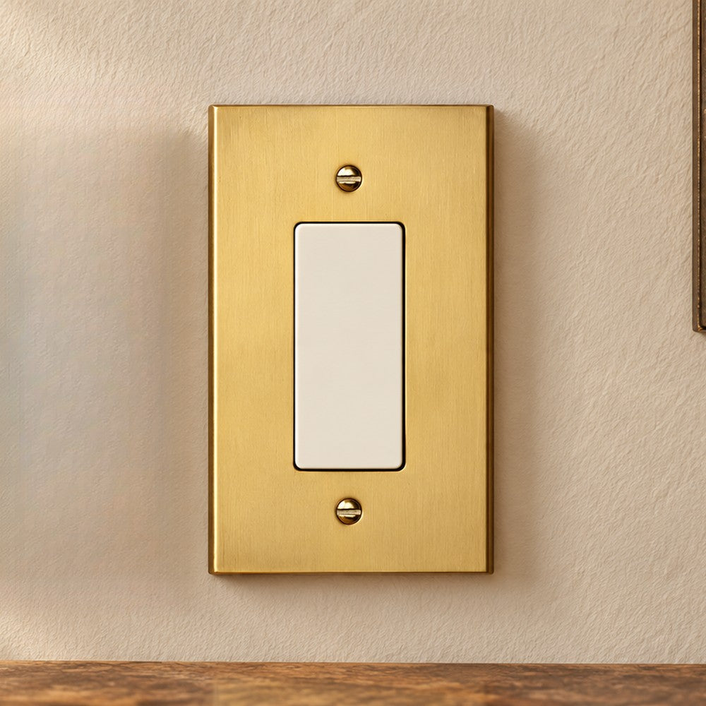 Brushed gold rocker switch plate on a warm white wall.