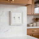 Estate 2-gang toggle switch plate in White on a light wall in a kitchen with a marble backsplash and wood cabinets