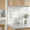 Estate 3-gang toggle switch plate in White on a light wall in a kitchen with white subway tile and wood cabinets