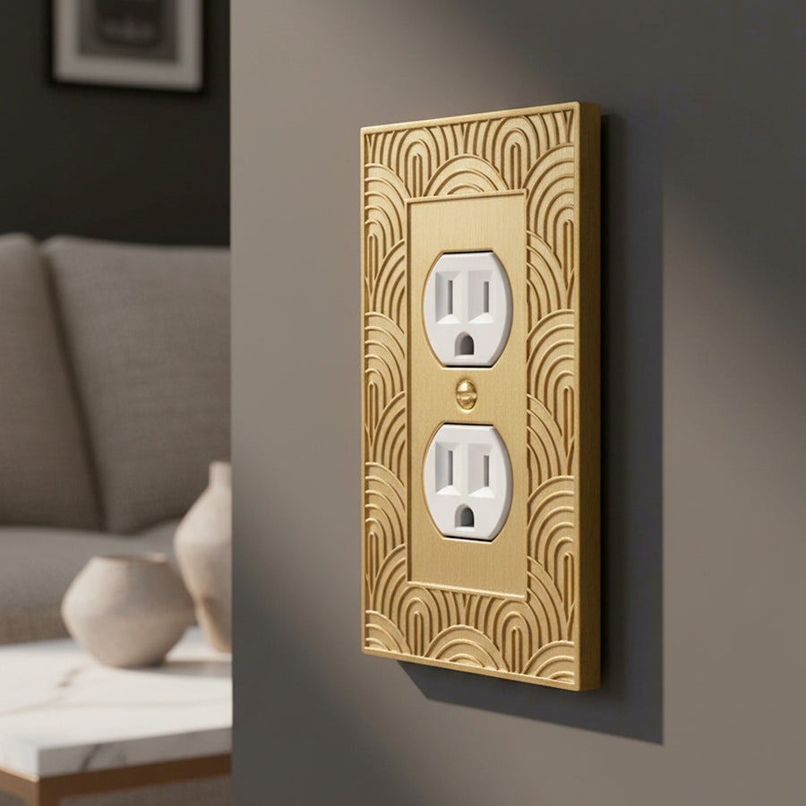 Gatsby duplex outlet cover in Brushed Gold on a charcoal living room wall