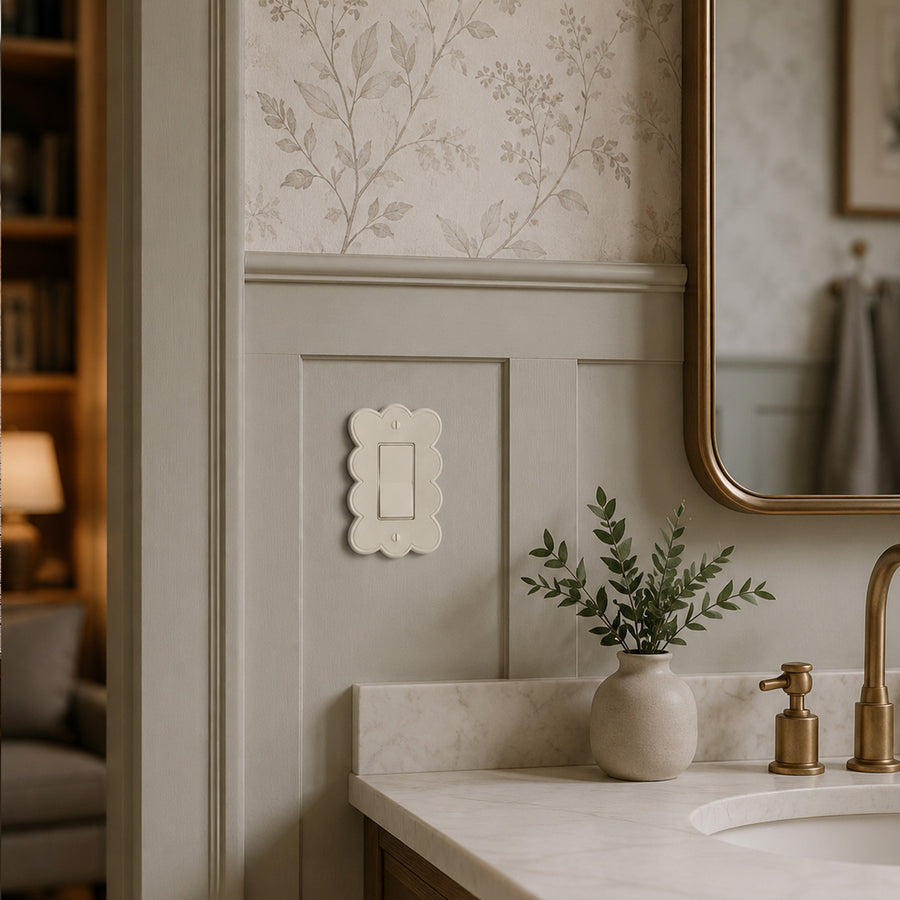 Scallop 1-gang rocker switch plate in Warm Ivory on a sage paneled bathroom wall above a marble vanity