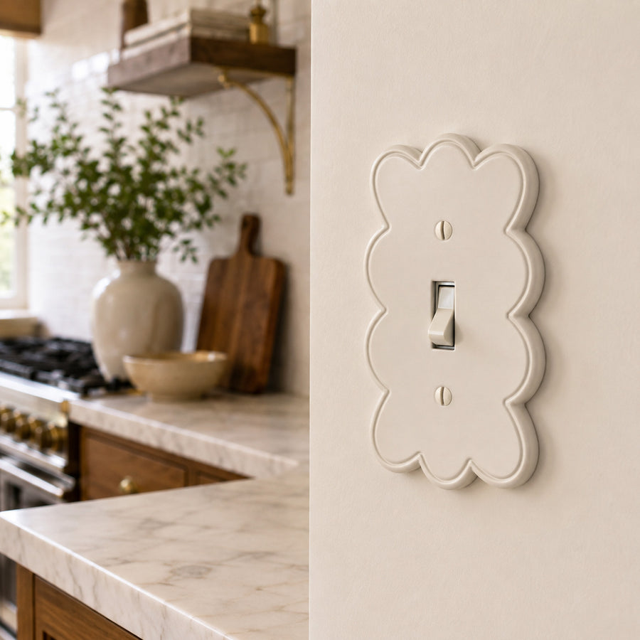 Scallop 1-gang toggle switch plate in Warm Ivory on a cream kitchen wall beside a marble counter