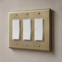 Signature 3-gang rocker switch plate in Aged Gold installed on a wall