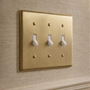 Signature 3-gang toggle switch plate in Aged Gold installed on a wall