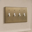 Signature 4-gang toggle switch plate in Aged Gold installed on a wall